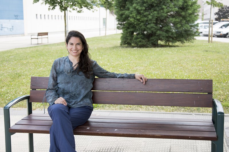 Foto de Marcela Vega sentada en un banco de madera